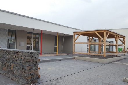 Foto des Eingangsbereichs der Kita, rechts der überdachte Abstellplatz für Kinderwagen. Quelle: Ausschreibung
