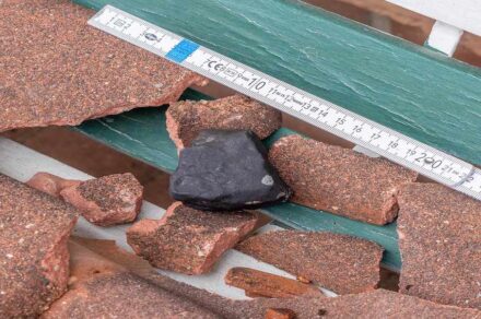 233,4 g schweres Fundstück des Meteoriten und die beschädigten Dachpfannen. Foto: Carsten Jonas, AKM