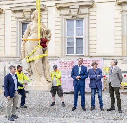 Die Skulpturen werden auf die Balustrade gehoben. (v.l.n.r.) Hermann Graser, Bamberger Natursteinwerk; (4. v.l.) Kulturstaatsminister Wolfram Weimer; (5.v.l.) Sven Schubert, Schubert Steinmetz und Steinbildhauer, Dresden; (6.v.l.) Professor Hartmut Dorgerloh, Generalintendant Humboldt Forum. Quelle: Stiftung Humboldt Forum im Berliner Schloss, Foto: David von Becker